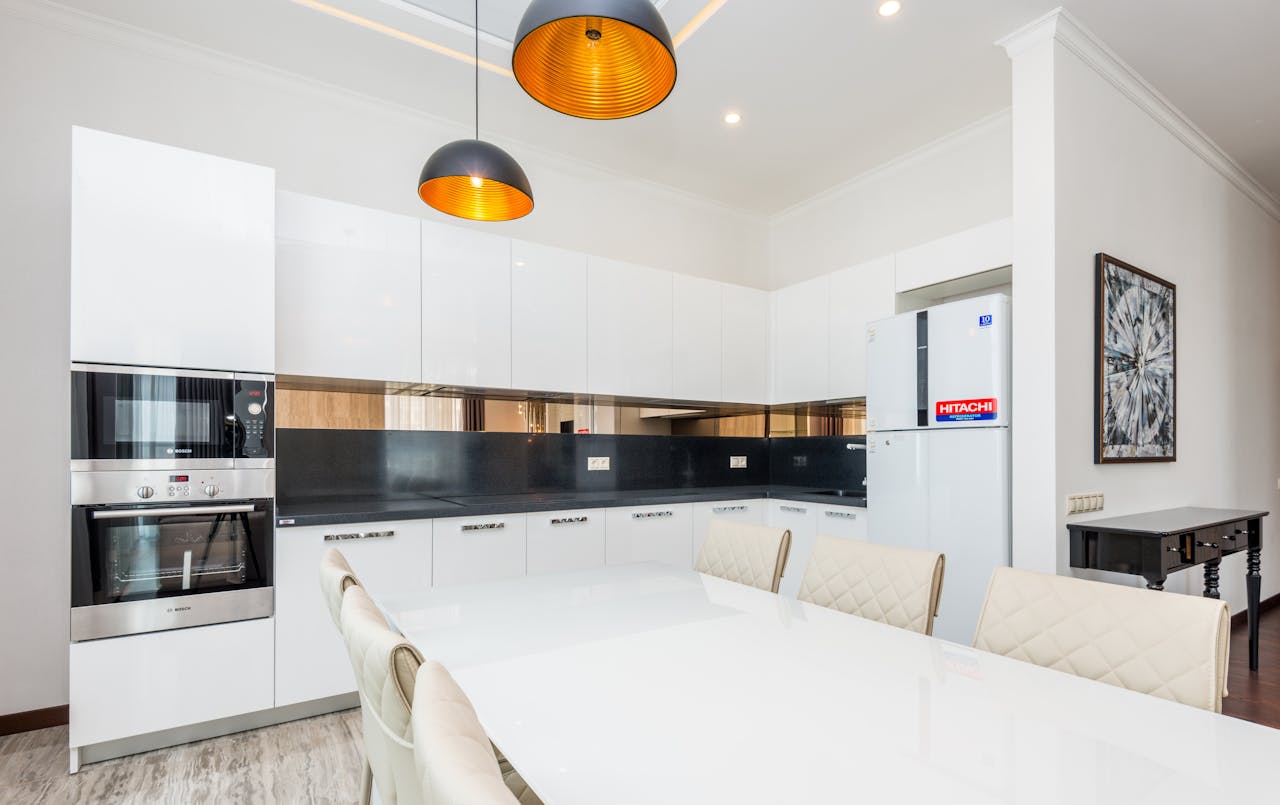 Elegant modern kitchen with white cabinets and sleek appliances featuring pendant lighting.
